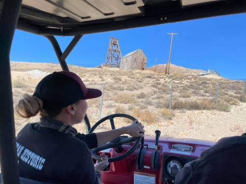 A person driving an off-road vehicle towards an old building on a hillside under a clear blue sky.