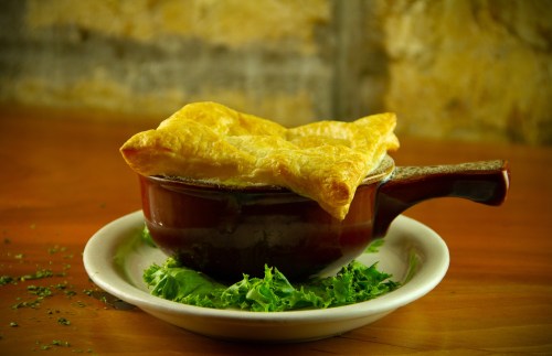 A golden-brown pastry atop a bowl, resting on a bed of fresh greens, set against a rustic background.