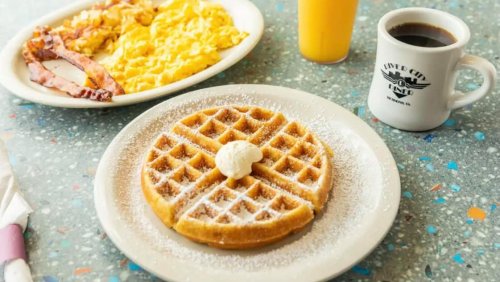 A plate of waffles topped with butter and powdered sugar, alongside a breakfast plate and drinks.