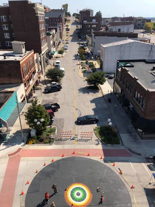 Aerial view of a street with a colorful circular design on the pavement and people working around it.
