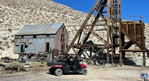 An old mining structure with a metal framework and a parked ATV in a desert landscape.