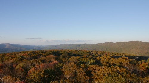 A panoramic view of rolling hills covered in autumn foliage under a clear blue sky.