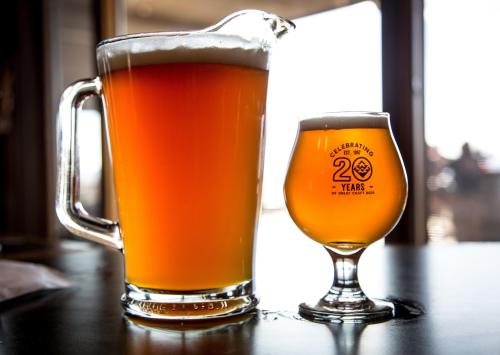 A large pitcher and a small glass of amber beer on a table, with a scenic background.