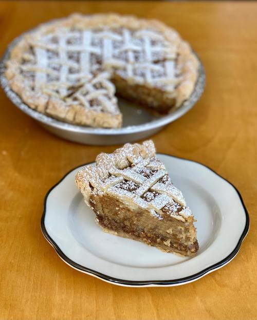 A slice of pie on a plate, with the whole pie in the background, both dusted with powdered sugar.