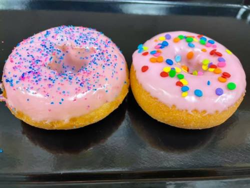 Two colorful donuts on a black plate: one with pink icing and sprinkles, the other with pink icing and colorful dots.
