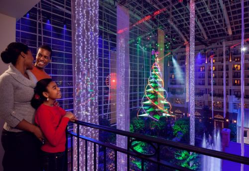 A family admires a colorful Christmas tree and festive lights in a beautifully decorated indoor space.