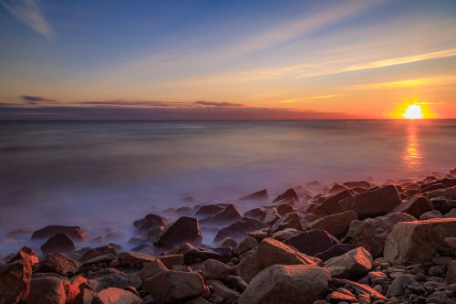 A serene sunset over the ocean, with soft waves lapping against rocky shores and colorful clouds in the sky.