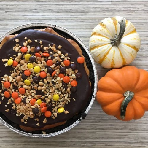 A chocolate dessert topped with candy and nuts, surrounded by small decorative pumpkins.