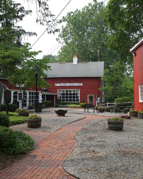 A charming red inn surrounded by greenery, with a brick pathway and outdoor seating area.