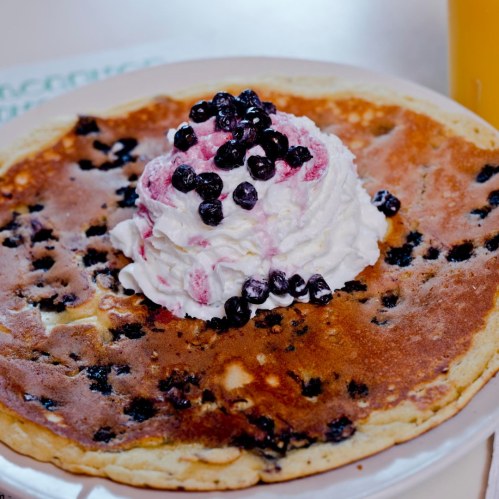 A large pancake topped with whipped cream and blueberries, served on a white plate.