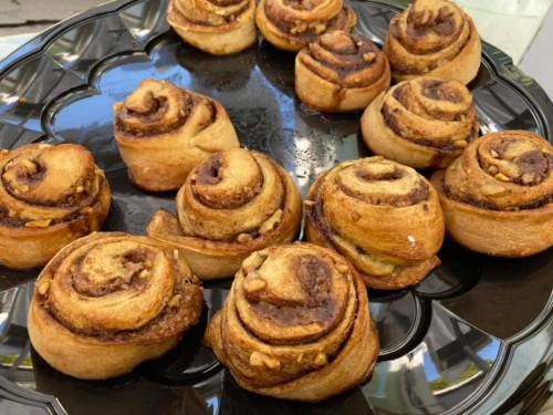 A black platter filled with freshly baked cinnamon rolls, golden brown and swirled with cinnamon and nuts.