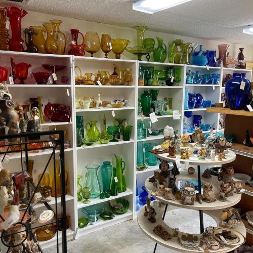 A display of colorful glassware and decorative items on shelves in a shop, featuring various shapes and sizes.