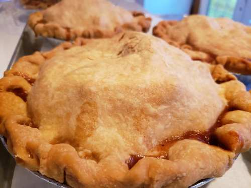 Three freshly baked pies with golden-brown crusts, slightly bubbling at the edges, on a silver baking tray.