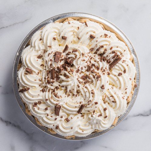 A creamy pie topped with swirls of whipped cream and chocolate shavings, set on a marble surface.