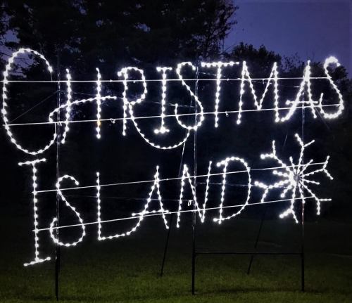 Bright white lights spell out "Christmas Island" with a snowflake on a dark background.