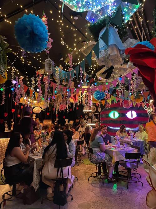 A vibrant restaurant interior filled with colorful decorations, string lights, and guests dining at tables.