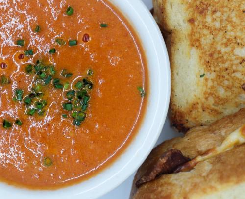 A bowl of tomato soup garnished with herbs, accompanied by a toasted sandwich.