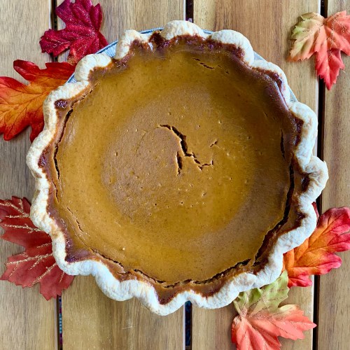 A freshly baked pumpkin pie on a wooden table, surrounded by colorful autumn leaves.