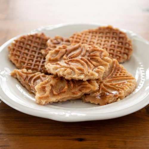 A white plate with several golden-brown, intricately patterned waffles arranged neatly.