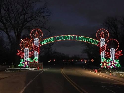Colorful holiday lights form an archway reading "Wayne County Lightfest," with candles and festive decorations.
