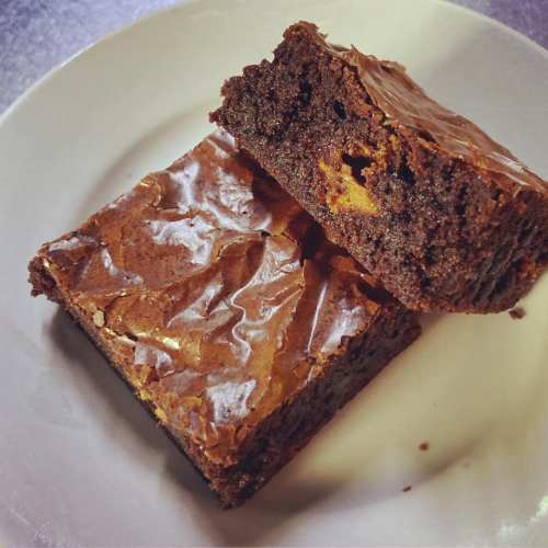 A close-up of a rich, fudgy brownie on a white plate, showcasing its shiny top and dense texture.