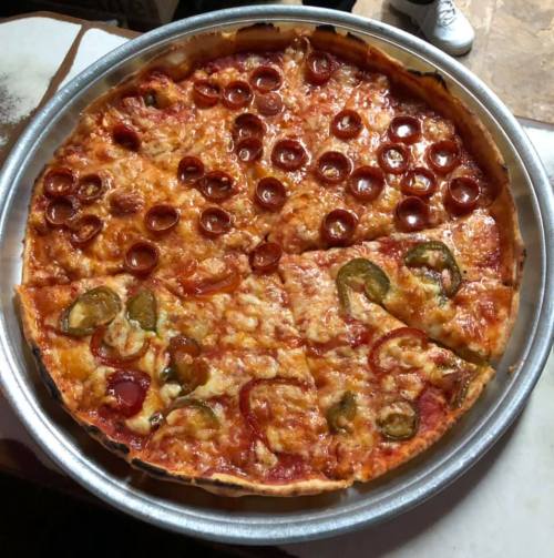A round pizza topped with pepperoni, green peppers, and melted cheese, served in a metal tray.