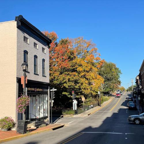 A quaint street scene with a shop, colorful autumn trees, and a clear blue sky.