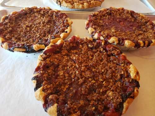 Three freshly baked fruit pies with crumbly topping, resting on a baking sheet.