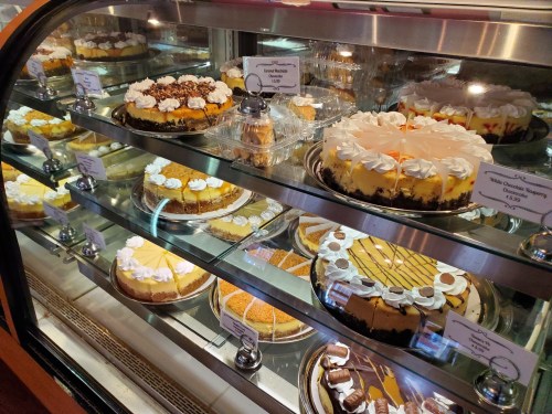 A display case filled with various cakes and desserts, including cheesecakes and layered cakes, all beautifully presented.