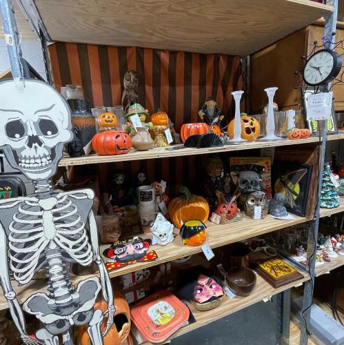 A display of Halloween decorations, including pumpkins, skeletons, and various themed items on wooden shelves.