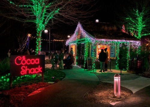 A cozy Cocoa Shack adorned with colorful lights, bustling with visitors on a festive night.