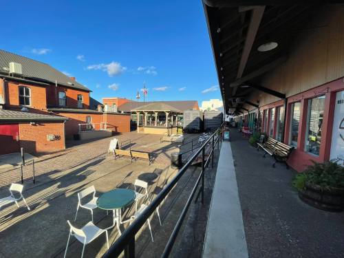 A sunny outdoor area with seating, tables, and buildings, under a clear blue sky.