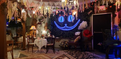 A whimsical room decorated with flowers, mirrors, and a glowing Cheshire Cat smile on the wall, creating a magical atmosphere.