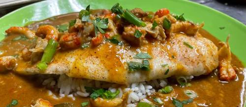 A plate of fish topped with a savory sauce, shrimp, and green onions, served over a bed of rice.