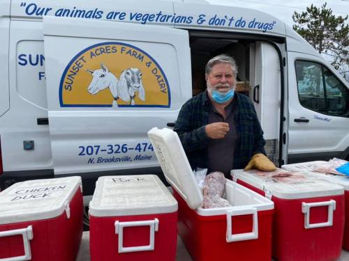 A man stands by a van with a farm logo, next to coolers filled with meat products, promoting a farm in Maine.