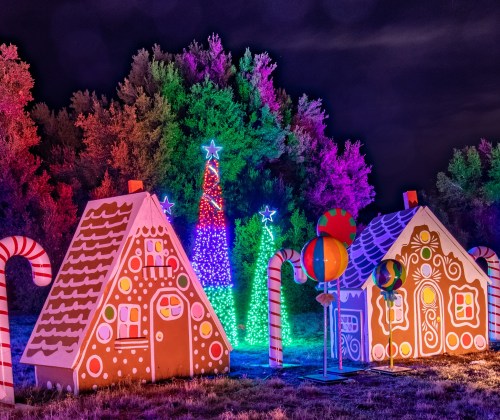 Colorful gingerbread houses and a lit tree surrounded by candy decorations in a festive nighttime setting.