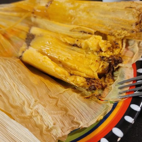 A close-up of a partially opened tamale, revealing yellow masa and chocolate filling, on a colorful plate.