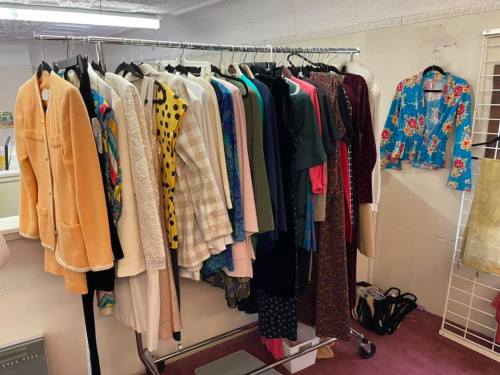 A clothing rack filled with various colorful garments, including jackets, dresses, and blouses, in a retail space.