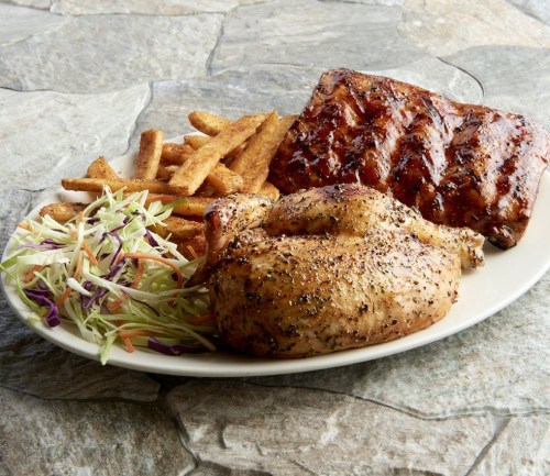 A plate featuring grilled chicken, BBQ ribs, fries, and coleslaw on a stone surface.