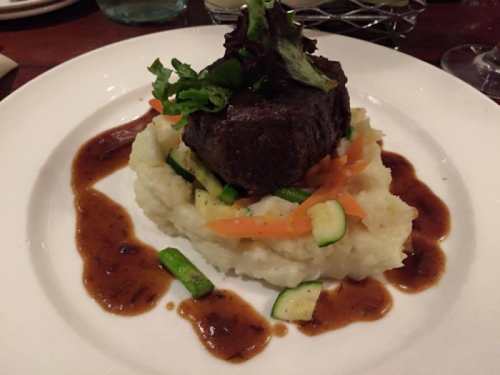 A plate featuring a beef filet atop creamy mashed potatoes, garnished with vegetables and a rich sauce.