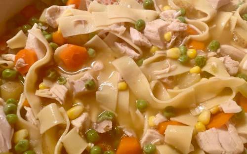 A close-up of a hearty chicken noodle soup with vegetables, including carrots, peas, and corn, in a savory broth.