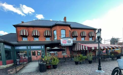 A brick building with striped awnings, outdoor seating, and potted plants, set against a clear blue sky.