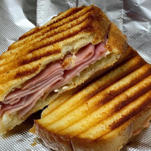 A toasted sandwich with layers of ham and cheese, cut in half, resting on a silver foil surface.