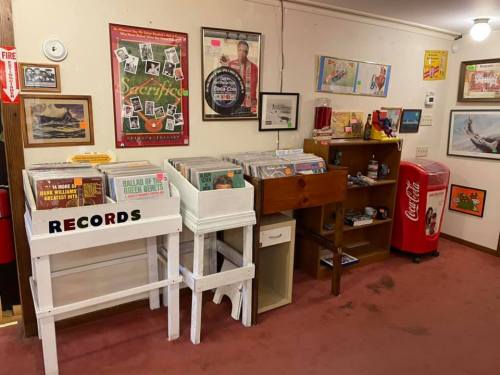 A cozy room with vintage decor, featuring record bins, a wooden cabinet, and a retro Coca-Cola fridge.