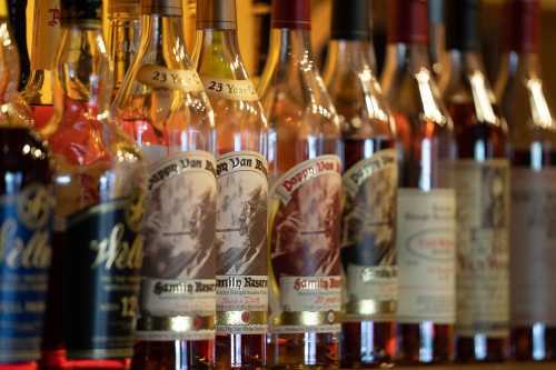 A close-up of various whiskey bottles lined up on a shelf, showcasing their labels and colors.