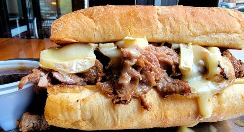 A close-up of a hearty sandwich filled with sliced beef and melted cheese on a toasted hoagie roll.