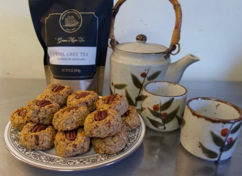 A plate of pecan cookies beside a teapot and two cups, with a bag of Earl Grey tea in the background.