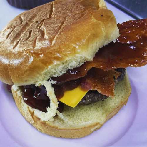 A close-up of a burger with a beef patty, cheddar cheese, bacon, and barbecue sauce on a soft bun.