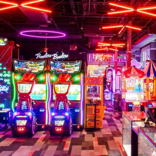 A vibrant arcade filled with colorful games and neon lights, featuring racing machines and various attractions.