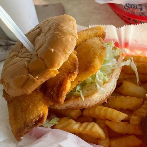 A close-up of a fried fish sandwich with lettuce, served with crinkle-cut fries on the side.